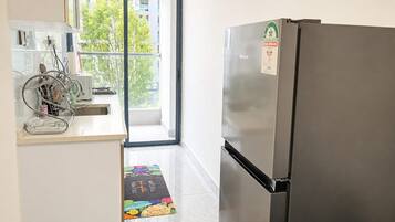 A kitchen with a stainless steel refrigerator, a dish rack, and a window with a view of buildings and trees.