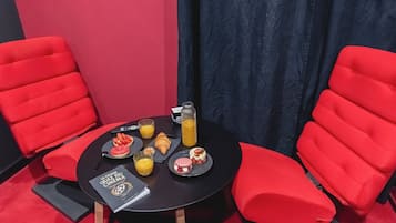 Ein kleiner runder Tisch mit einem Buch, einem Glas Orangensaft, einer Saftflasche und verschiedenen Backwaren.