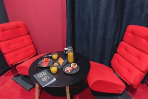 Uma pequena mesa redonda com um livro, um copo de sumo de laranja, uma garrafa de sumo e vários doces.