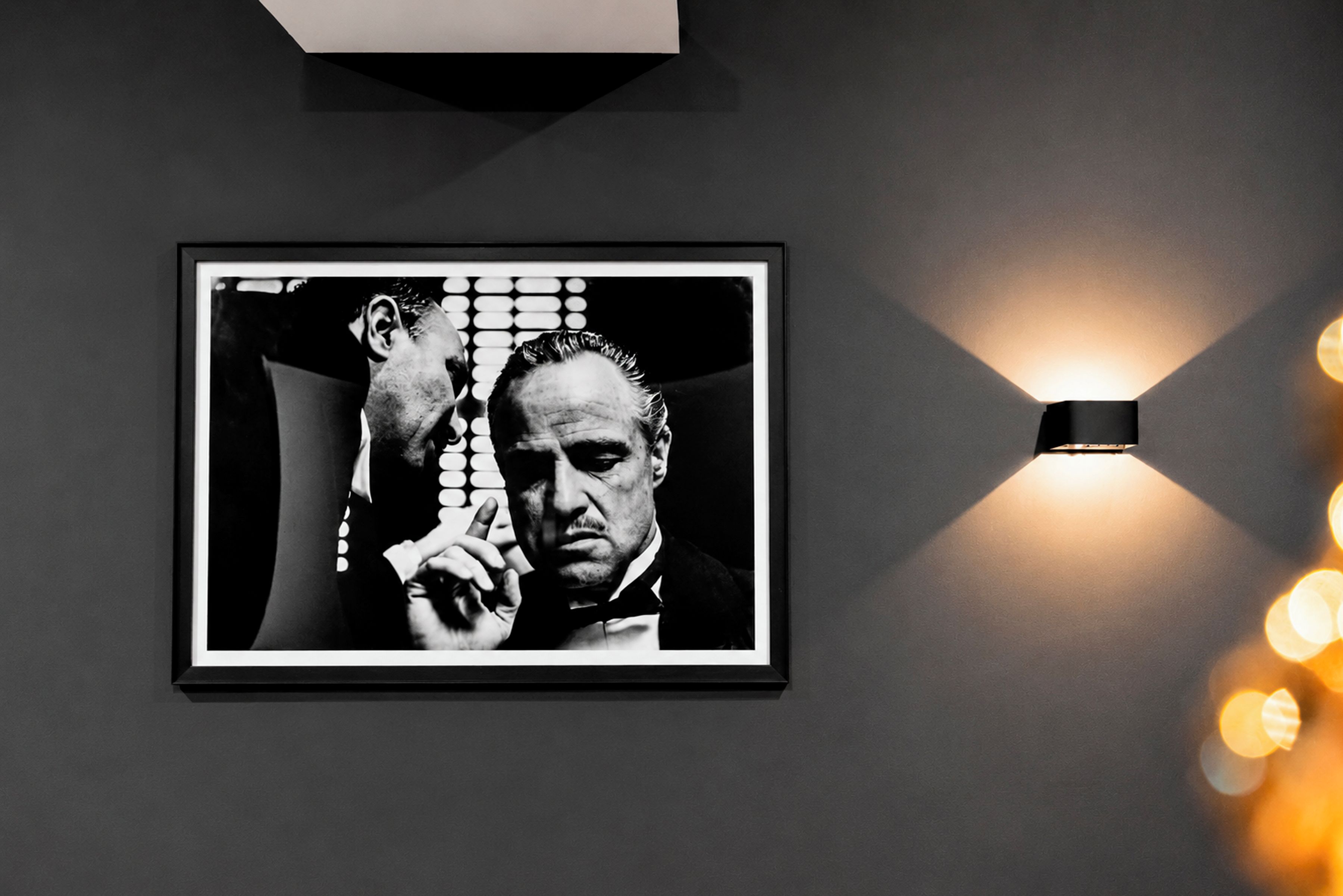 Une photographie en noir et blanc, encadrée, est accrochée au mur, et une applique murale moderne se trouve à sa droite.