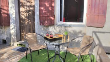 Eine Terrasse mit zwei Korbstühlen, einem Tisch und einem Fenster mit Rollläden.