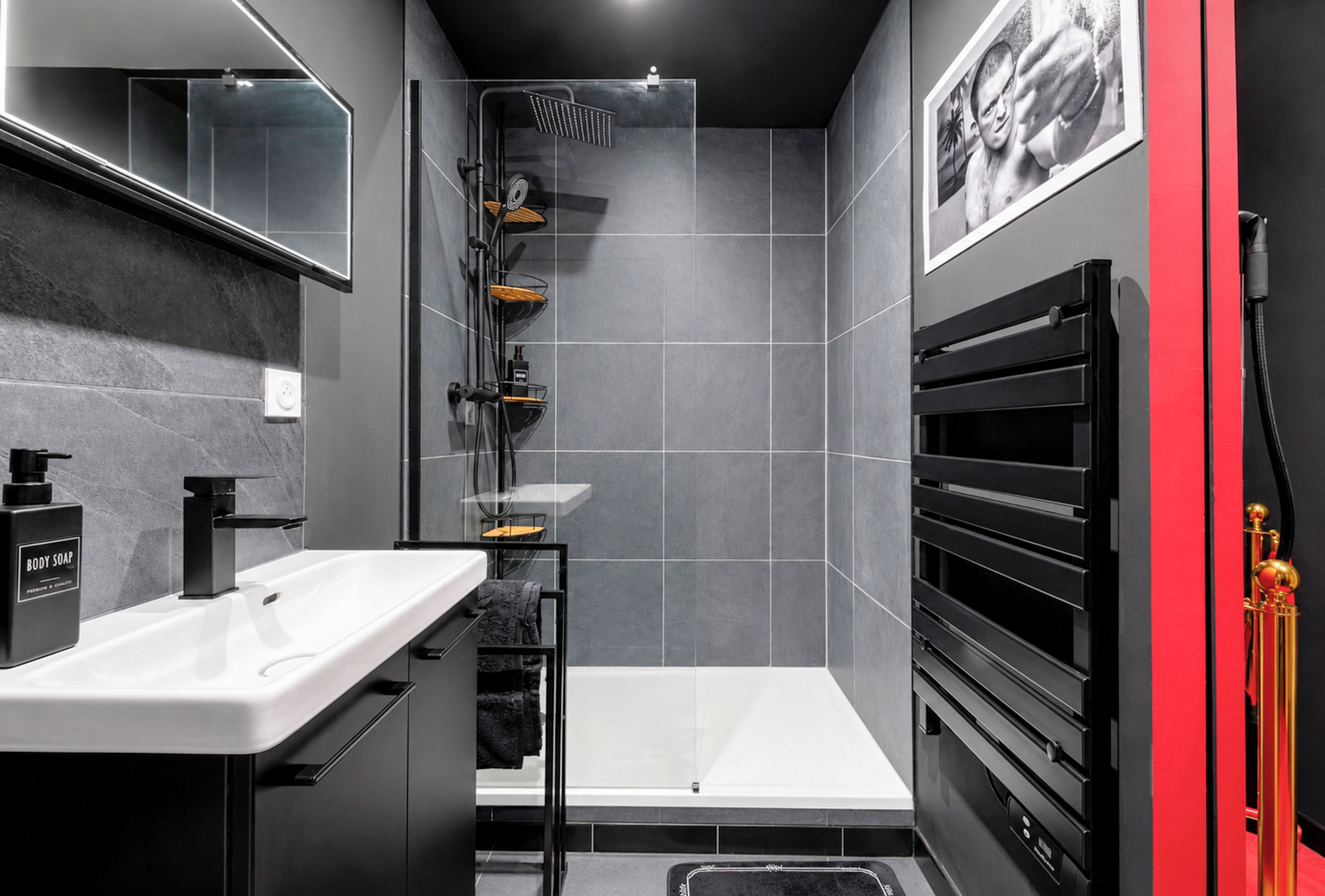 A modern bathroom with a white sink, black fixtures, a shower with a rain showerhead, and a red accent wall.