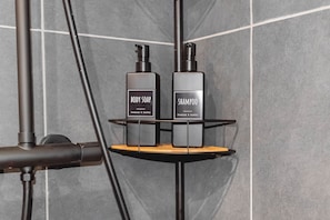 A bathroom with a shower head, a black towel rack, and two bottles of body soap and shampoo. - Le Prestige - Movie Room, Netflix, Downtown (Angers)