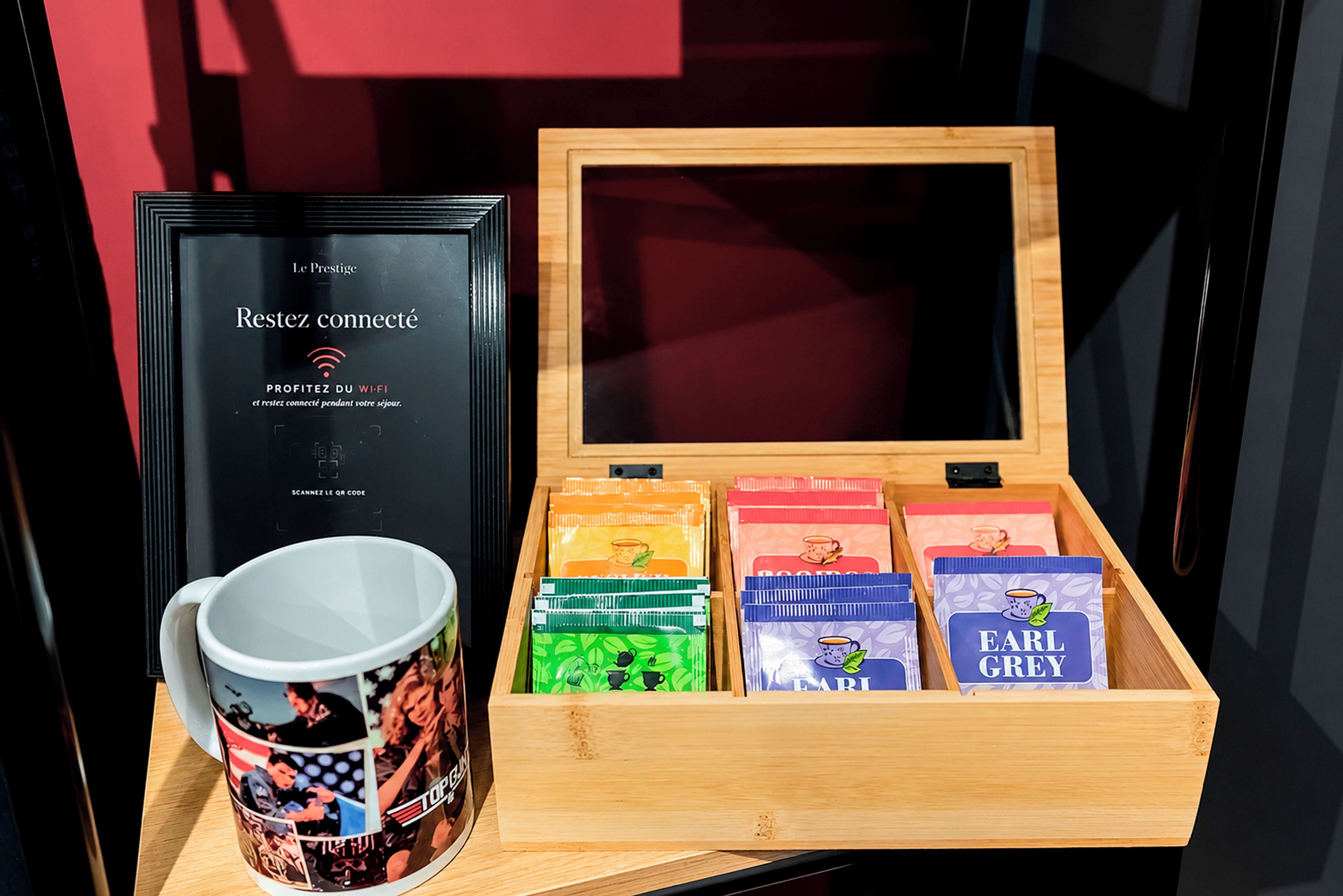 Une boîte en bois contenant des sachets de thé et une tasse ornée d’une publicité pour du café.