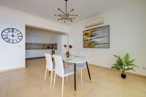 A modern kitchen with white cabinets, a microwave, and a dining area with a glass table and white chairs. - Oceanview Luxury, Fort Cambridge W/pool (Sliema)