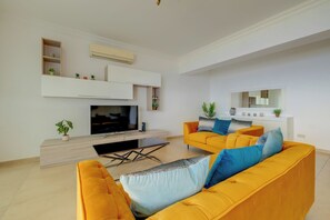 A modern living room with a flat-screen TV, two yellow sofas, a coffee table, and a white entertainment unit. - Oceanview Luxury, Fort Cambridge W/pool (Sliema)