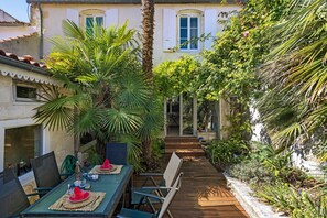 A patio with a table set for dining, surrounded by lush greenery and a palm tree. - Bed and Breakfast 'Suite La Tête Dans Les Étoiles' with Shared Terrace and Wi-Fi (La Rochelle)