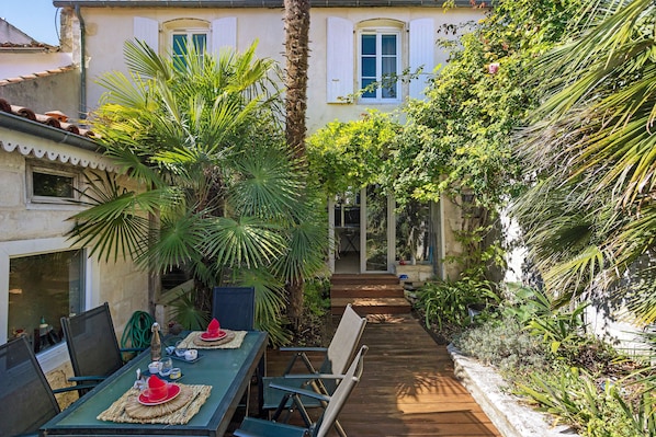 A patio with a table set for dining, surrounded by lush greenery and a palm tree.