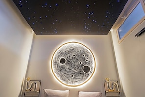 A room with a starry ceiling, a circular moon-like artwork, and two framed decorative items.