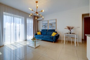 Un saló modern amb un sofà blau, una taula de centre de vidre i una zona de menjador amb taula i cadires blanques.