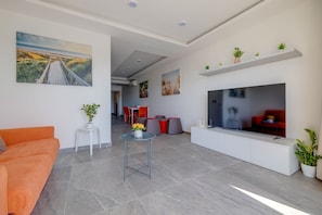 A modern living room with a flat-screen TV, a dining area with red chairs, and a sofa. - Idyllic Apartment With Valletta and Harbour Views (Gzira)