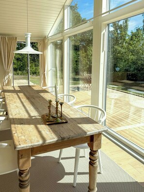 Een houten eettafel met kandelaars, witte stoelen en grote ramen met uitzicht op de omgeving.