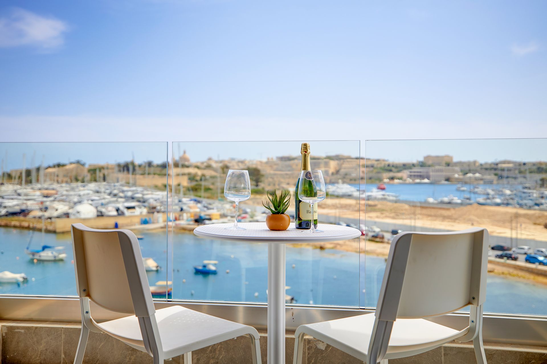 A balcony with a table set for two, overlooking a marina with boats.