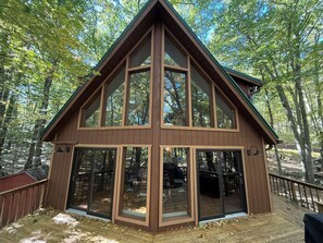 A cabin with a large glass front, wooden deck, and a steeply pitched roof. - Spacious 3-Bedroom Retreat in the Poconos - WLE Amenities (Lake Ariel)