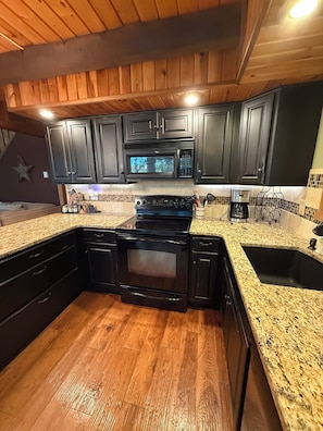A kitchen with dark cabinets, a granite countertop, a stove, a microwave, and a coffee maker. - Spacious 3-Bedroom Retreat in the Poconos - WLE Amenities (Lake Ariel)