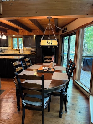 A dining area with a wooden table and chairs, a hanging light fixture, and a view of the outdoors through large windows. - Spacious 3-Bedroom Retreat in the Poconos - WLE Amenities (Lake Ariel)