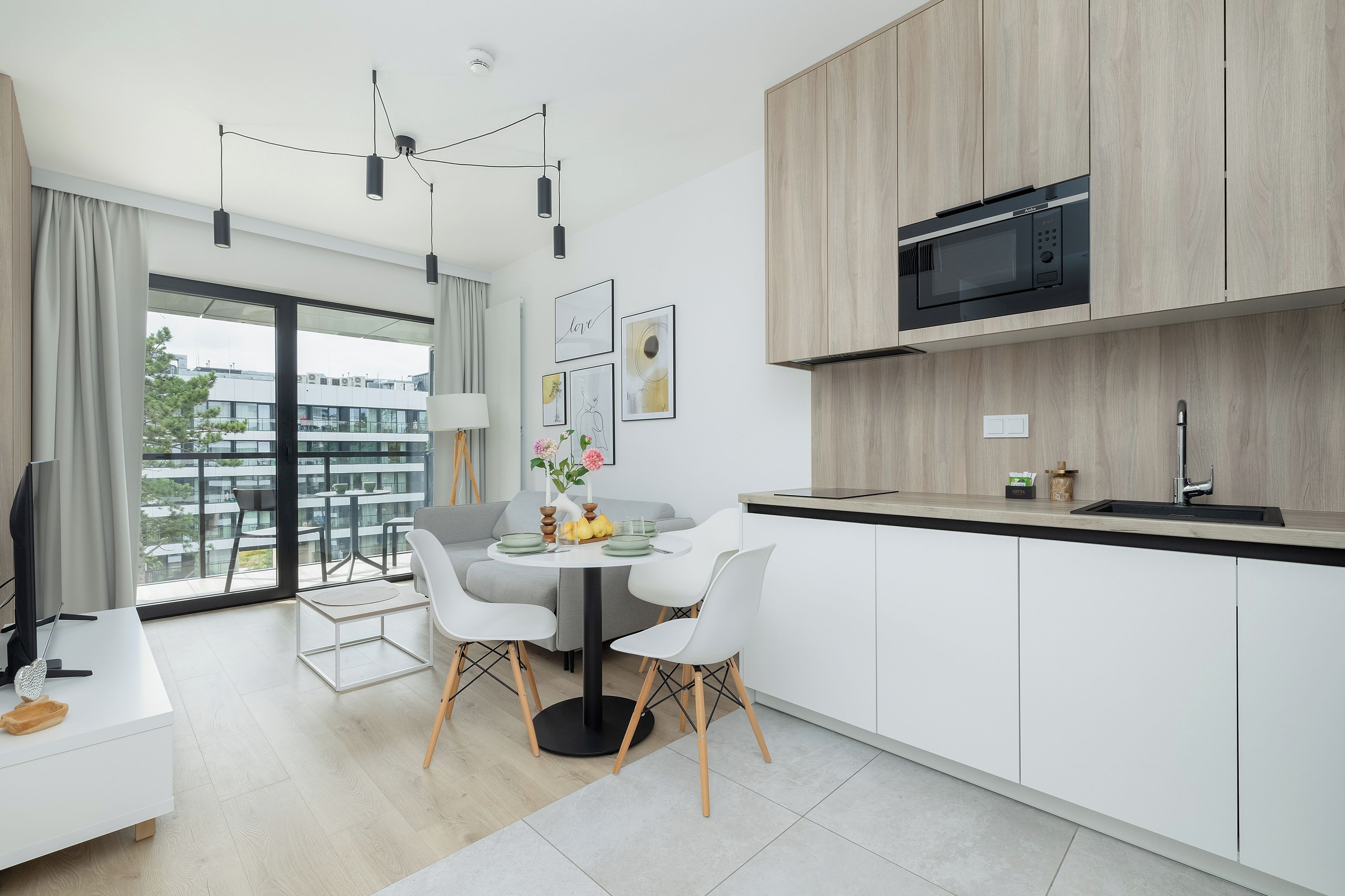 Et moderne køkken med indbygget mikroovn, et spiseområde med et rundt bord og stole, samt udsigt til en balkon med bybillede.