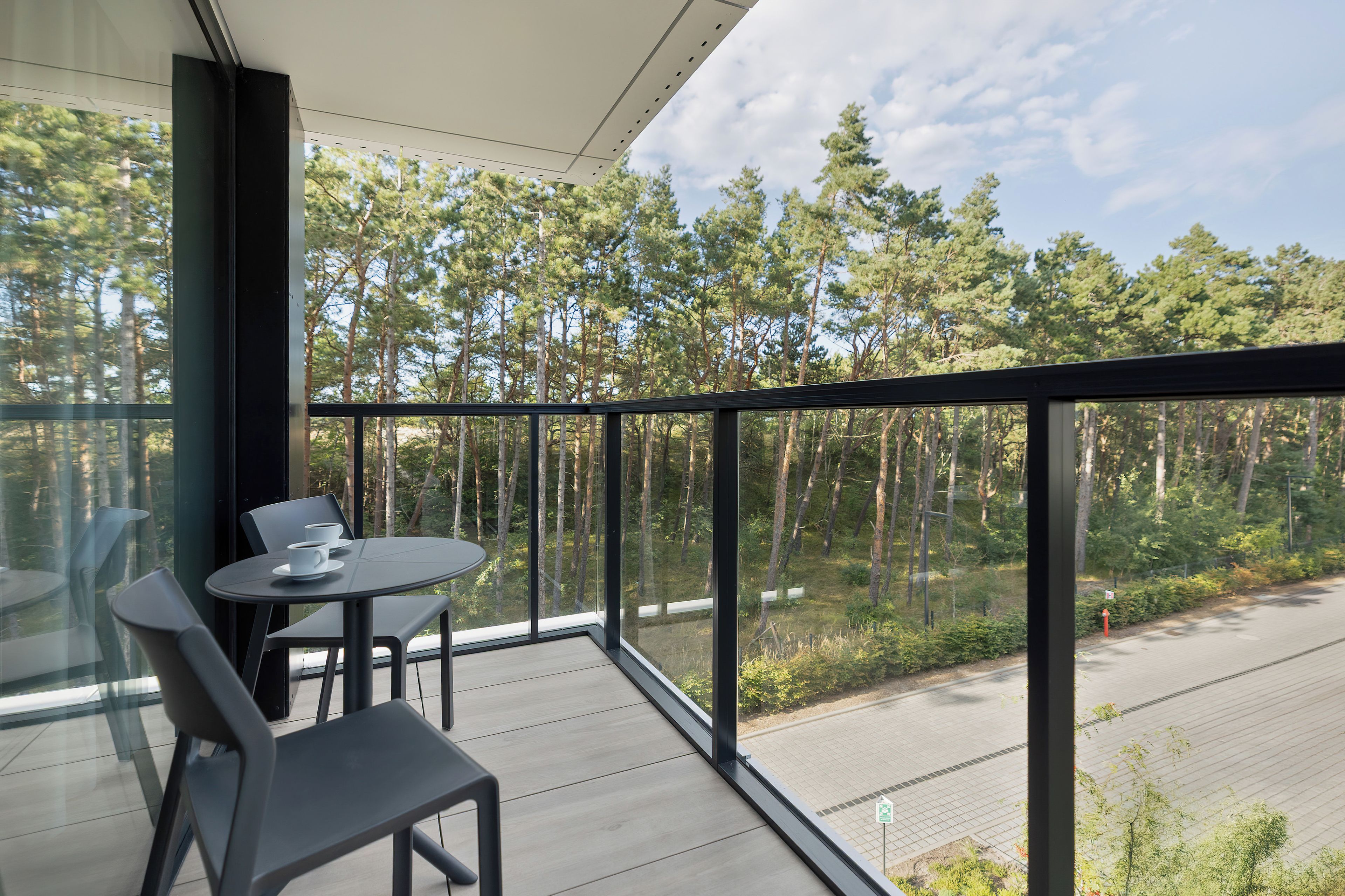 A balcony with a table and chairs, overlooking a forested area.