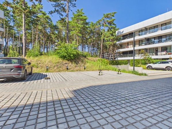 A paved area with cars parked, surrounded by trees and a modern building with balconies. - Hotel Shellter Resort & Spa (Rogowo)