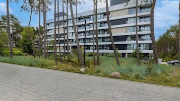 En moderne boligbygning med flere etager og altaner, omgivet af en anlagt have med træer og buske.