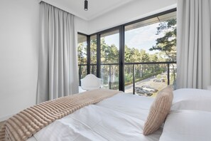 A modern hotel room with a large window, a bed with white linens, a beige throw blanket, and a white chair. - Hotel Shellter Resort & Spa (Rogowo)