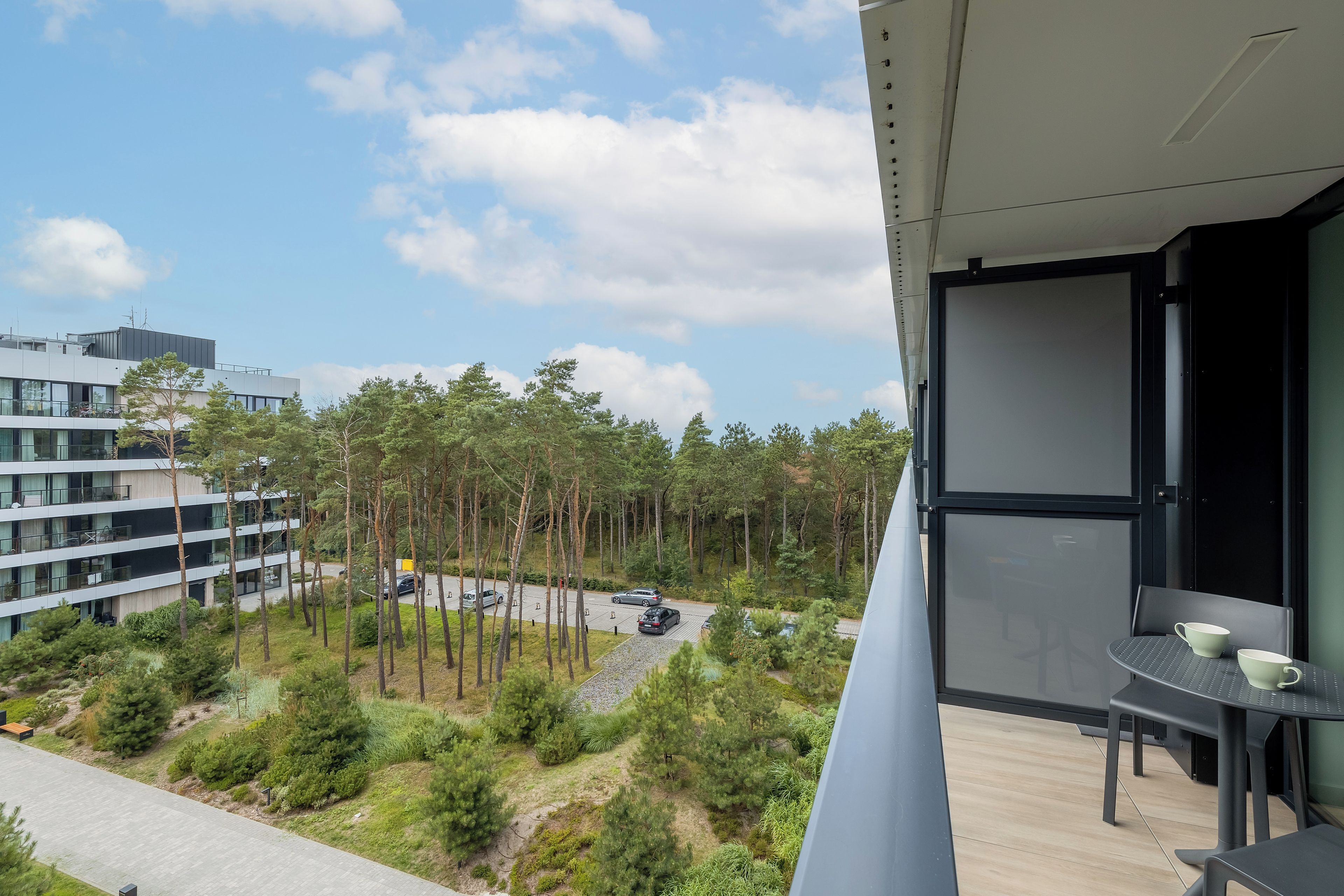 Ein Balkon mit Tisch und Stühlen, mit Blick auf einen Parkplatz und ein mehrgeschossiges Gebäude.