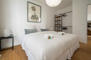 Ein modernes Schlafzimmer mit einem großen Bett, einem Nachttisch mit Lampe, einem Kleiderständer und einem gerahmten Kunstwerk an der Wand.