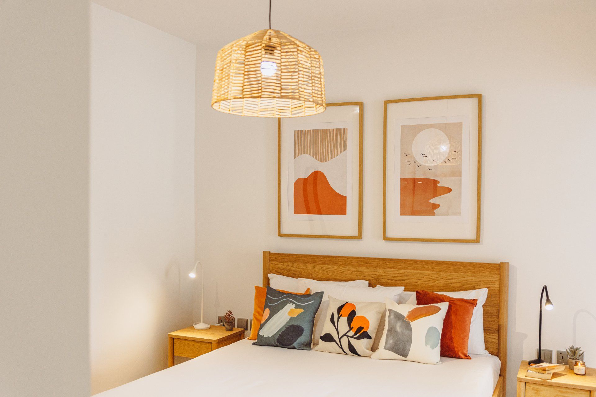 A bedroom with a wooden headboard, a hanging woven light fixture, and two framed abstract paintings.