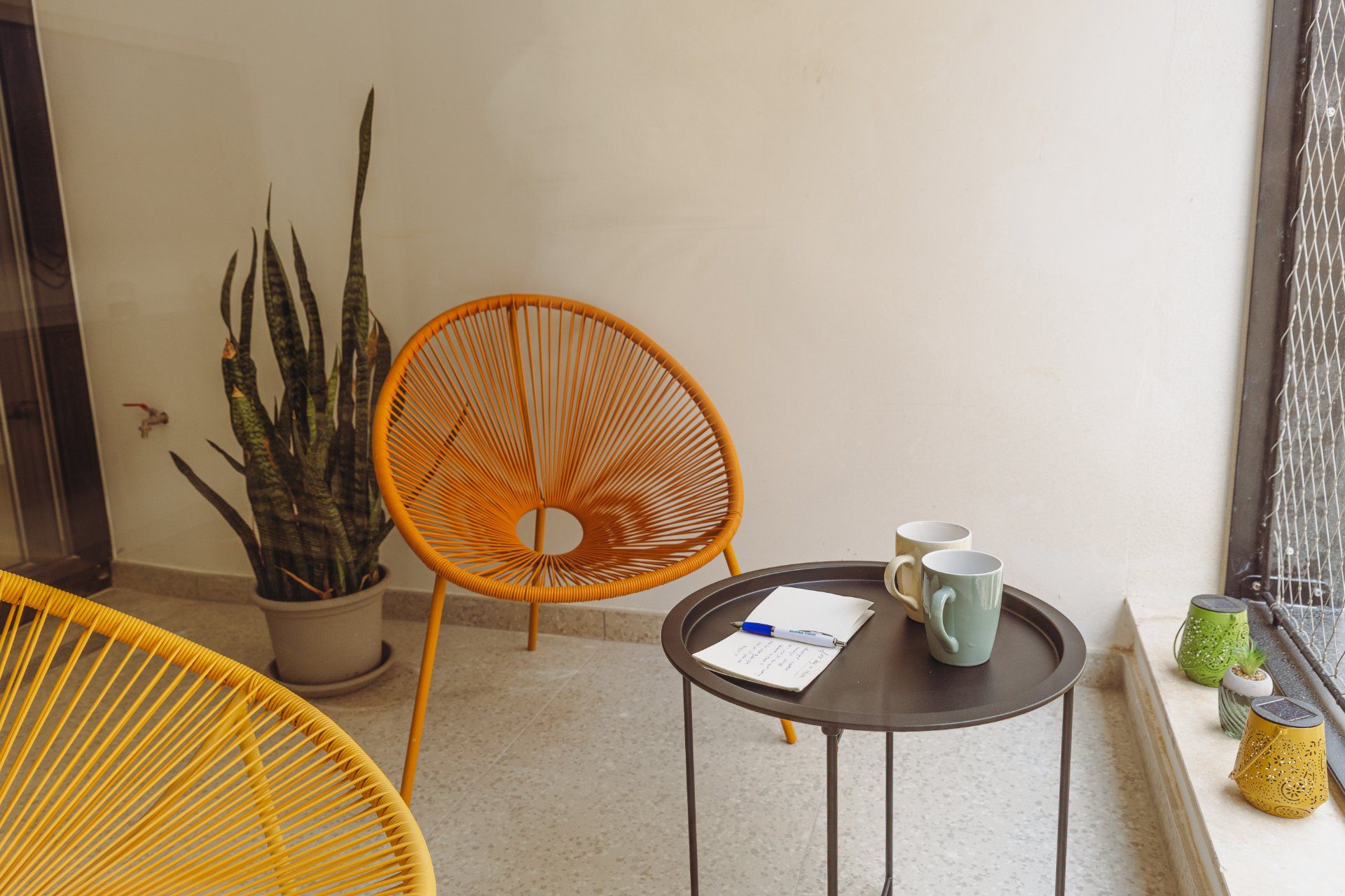 A small, round table with a notebook and pen, a chair, and a potted plant in a corner.