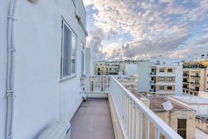 Ein Balkon mit Blick auf umliegende Gebäude und einen bewölkten Himmel.