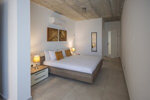 A bedroom with a bed, bedside tables, a wall-mounted air conditioner, and artwork.