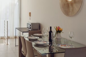 A dining area with a glass table, chairs, plates, wine glasses, and a vase with flowers.