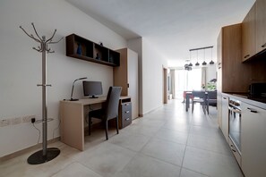 A modern kitchen with a dining area, a coat rack, and a workspace with a computer. - Charming Central Apartment, Your Perfect Getaway (Msida)