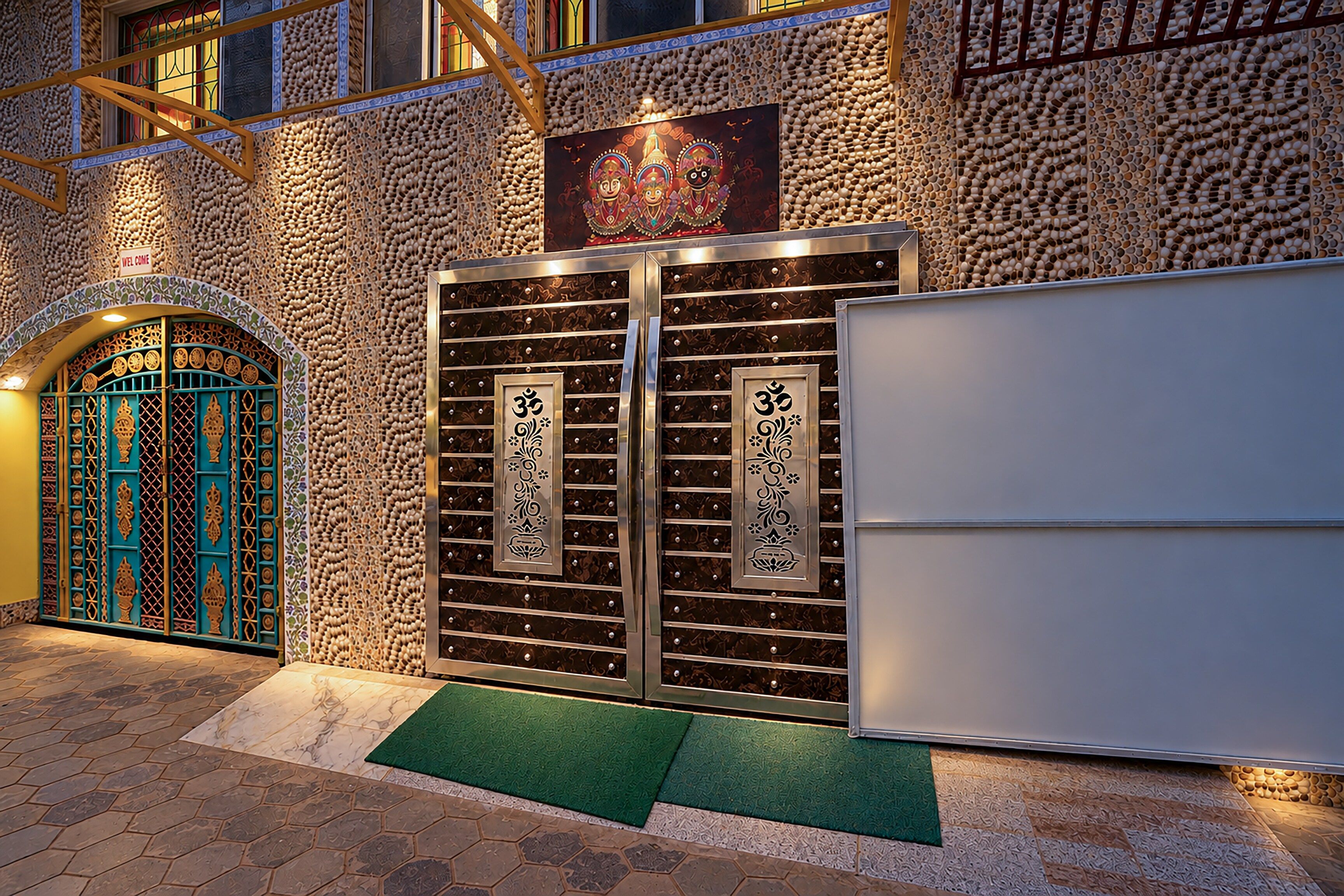 A traditional building with a large, ornate gate featuring religious symbols, a welcoming sign, and a modern door.