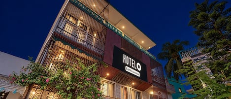Um hotel com vários andares, um letreiro chamativo com a palavra 'HOTEL', varandas e vasos de plantas.