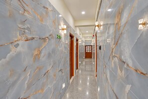 Un couloir en marbre, avec un panneau indiquant la sortie de secours, des portes et des luminaires fixés au mur.