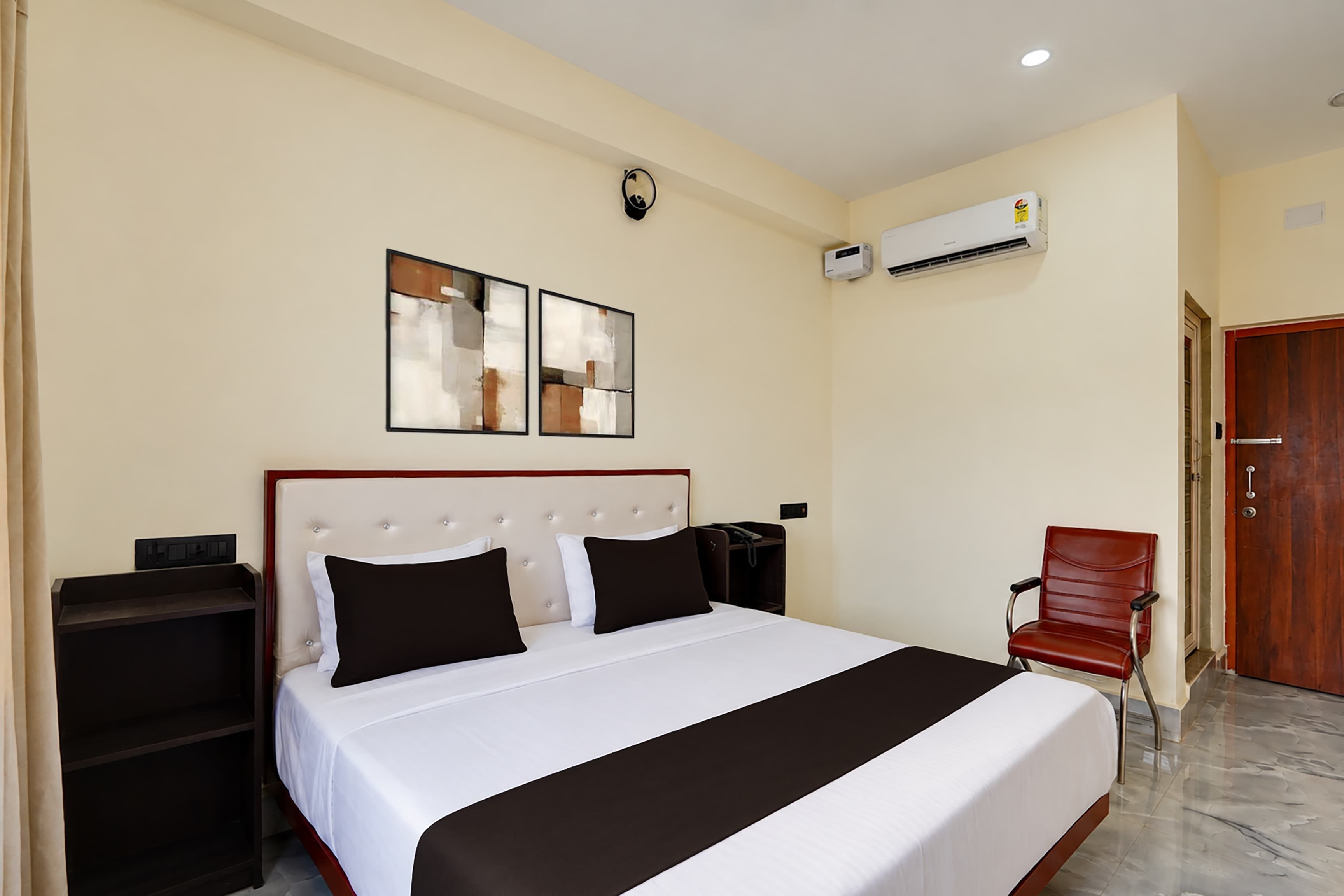 Een hotelkamer met een bed, nachtkastjes, een stoel, een airconditioning en een deur.