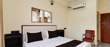 A hotel room with a bed, bedside tables, a chair, an air conditioning unit, and a door.