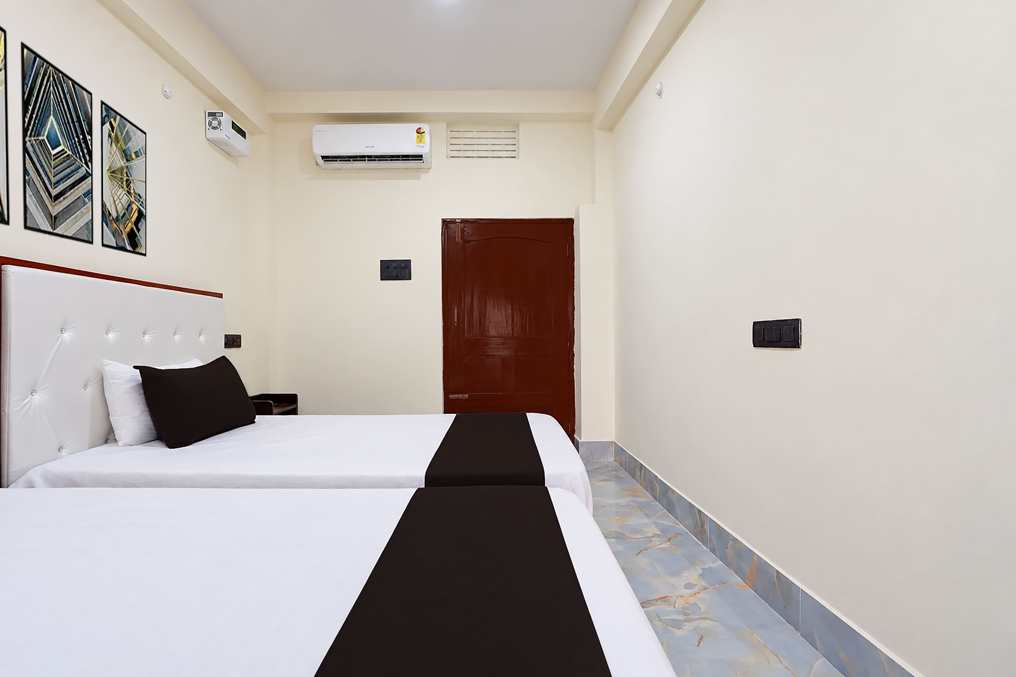Habitación de hotel con dos camas, una puerta de madera y un equipo de aire acondicionado en la pared.