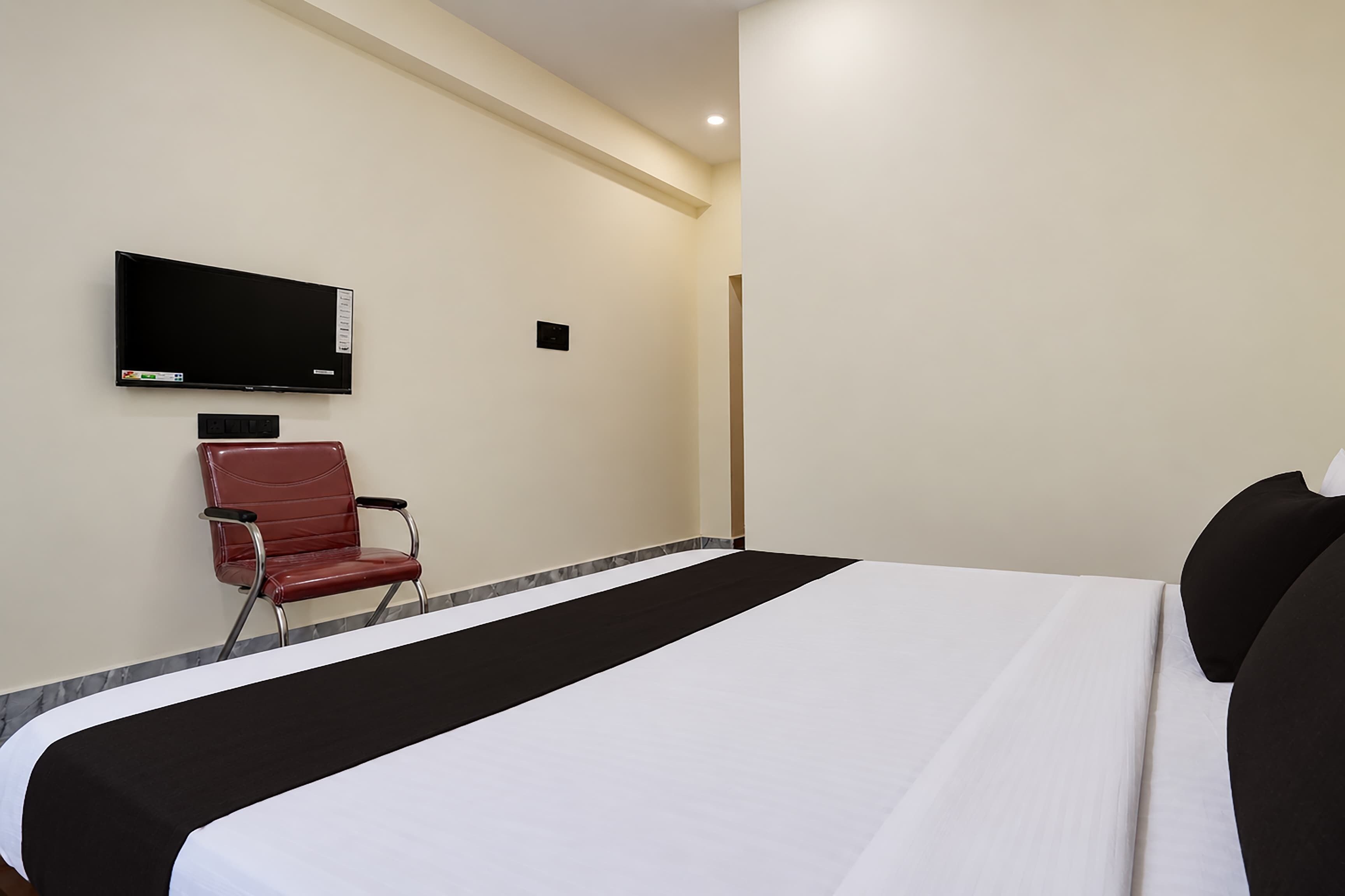 A hotel room with a bed, a TV mounted on the wall, and a chair.