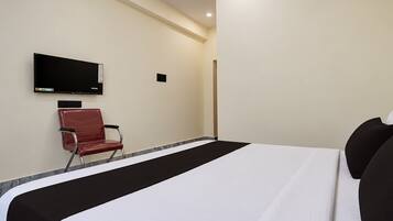 A hotel room with a bed, a TV mounted on the wall, and a chair.
