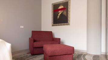Quarto com poltrona e banqueta vermelhas, um retrato emoldurado na parede e um tapete estampado.