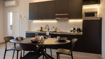 Una cocina moderna con armarios oscuros, una isla central y una zona de comedor con cuatro sillas.