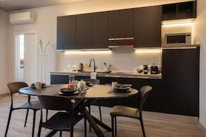 A modern kitchen with dark cabinetry, a central island, and a dining area with four chairs. - LOFT ZAI (Verona)
