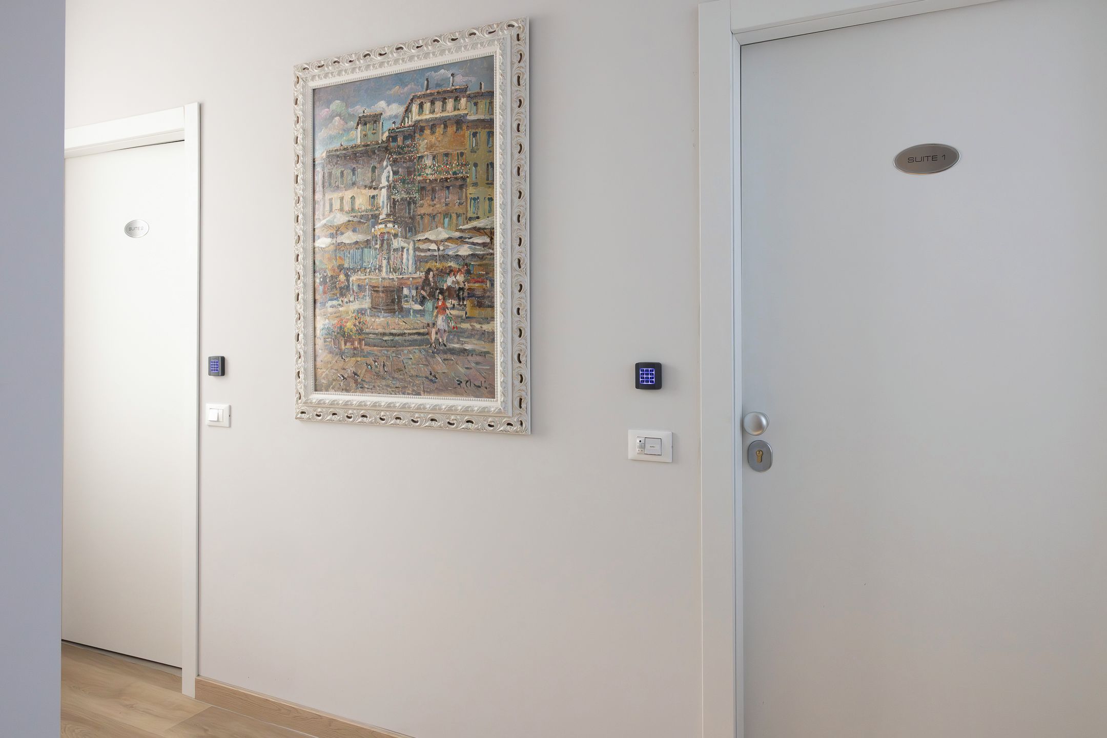 A hotel corridor with a framed painting of a cityscape, a door labeled 'SUITE 1', and a keycard reader.