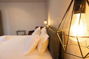 A neatly made bed with white linens and pillows, a geometric wall-mounted light fixture, and a small table with a chair in the background. - LOFT ZAI (Verona)
