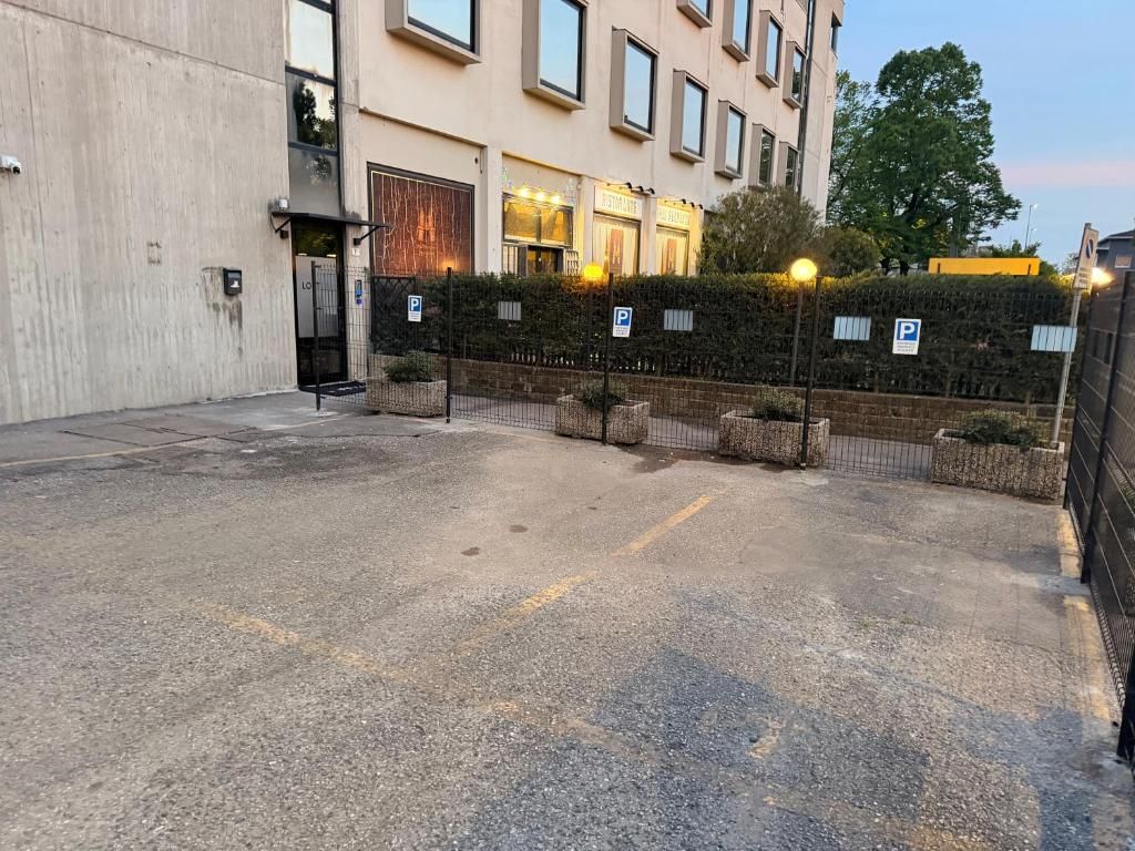 Ein Parkplatz mit befestigtem Eingang, ein Gebäude mit beleuchteten Fenstern und ein Baum im Hintergrund.