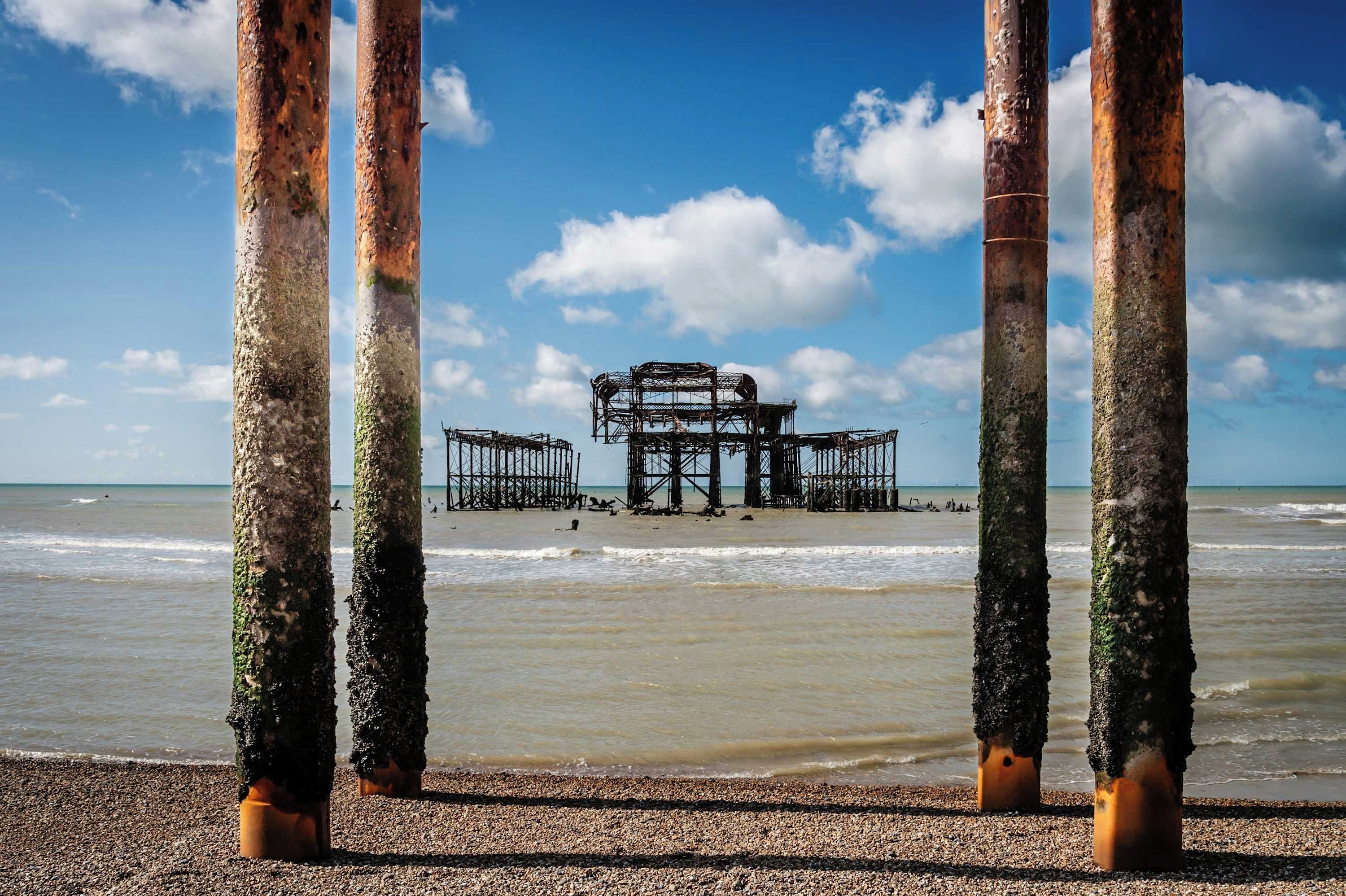 A beach with a structure in the background, viewed through rusted poles.