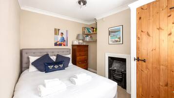 A relaxed, airy second bedroom with practical storage and a feature fireplace adding period character. Thoughtful artwork, good natural light, and comfortable bedding create a warm, calm space that feels quietly stylish and easy to unwind in.