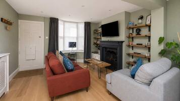 A living room with a fireplace, a television mounted above it, and a sofa with cushions.